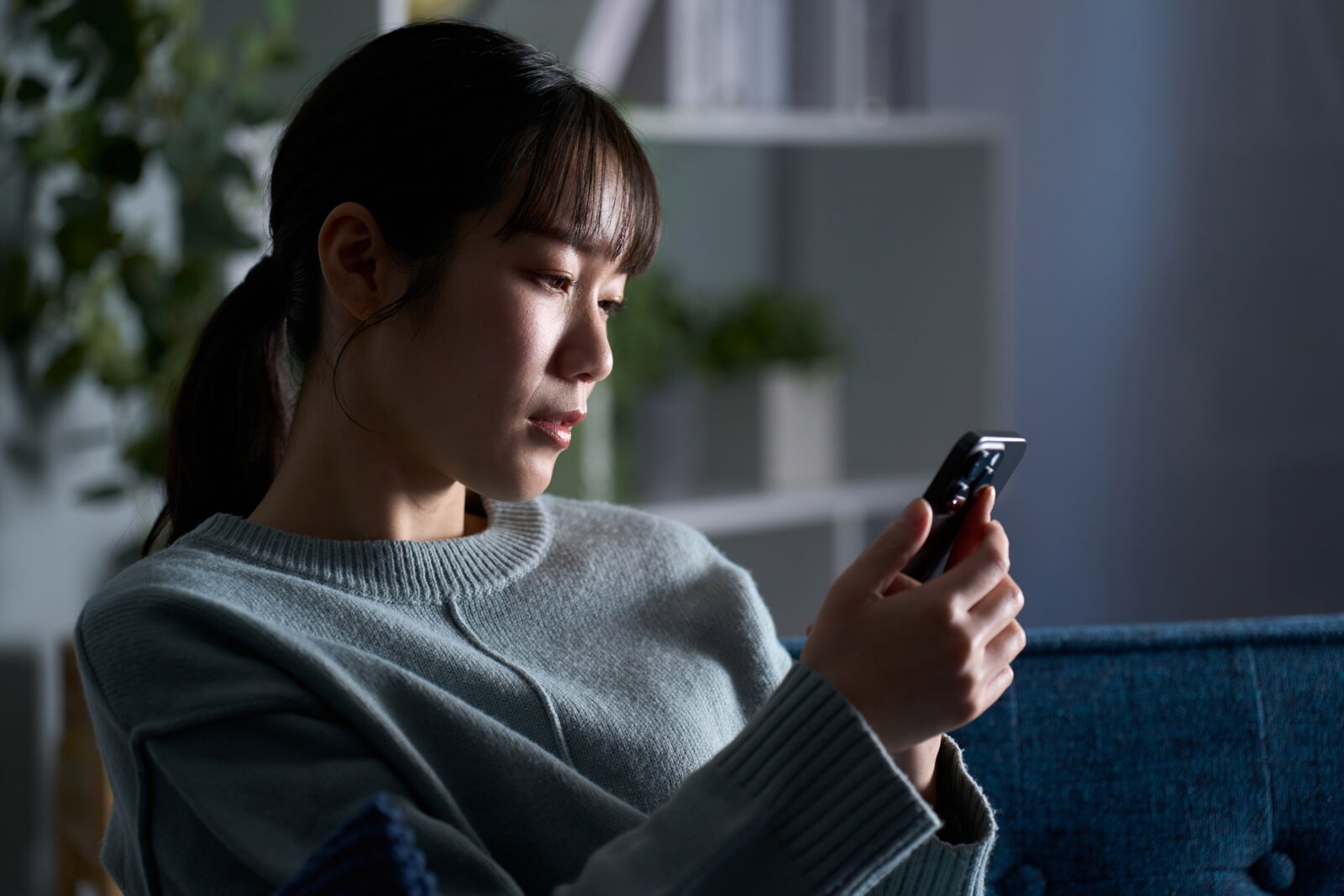 不安でスマホを見つめる女性